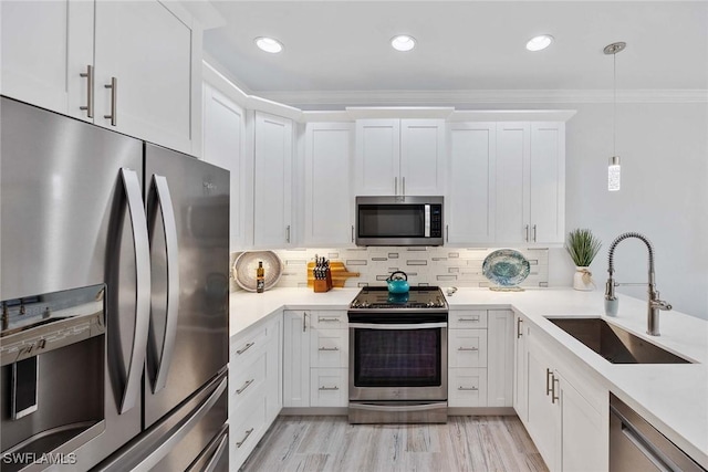 kitchen featuring white cabinets, crown molding, sink, hanging light fixtures, and stainless steel appliances