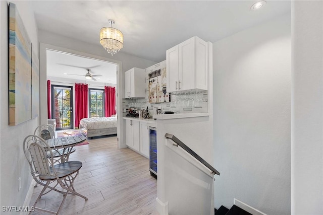 kitchen featuring wine cooler, backsplash, white cabinets, ceiling fan with notable chandelier, and light wood-type flooring