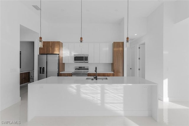 kitchen featuring sink, pendant lighting, a kitchen island with sink, white cabinets, and appliances with stainless steel finishes