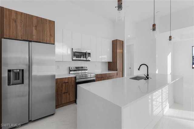 kitchen with appliances with stainless steel finishes, sink, decorative light fixtures, a center island with sink, and white cabinets