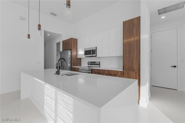 kitchen with a center island with sink, sink, hanging light fixtures, appliances with stainless steel finishes, and white cabinetry