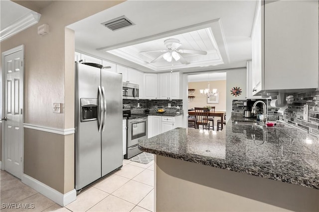 kitchen with dark stone counters, white cabinets, a tray ceiling, kitchen peninsula, and stainless steel appliances