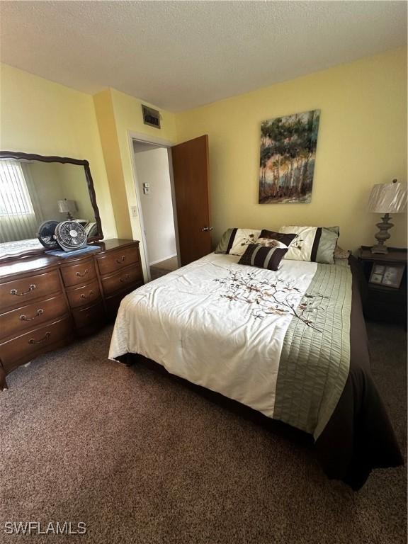 bedroom with a textured ceiling and dark colored carpet