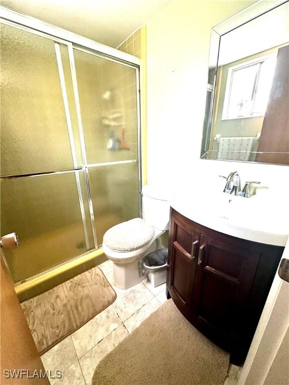 bathroom with tile patterned floors, vanity, an enclosed shower, and toilet