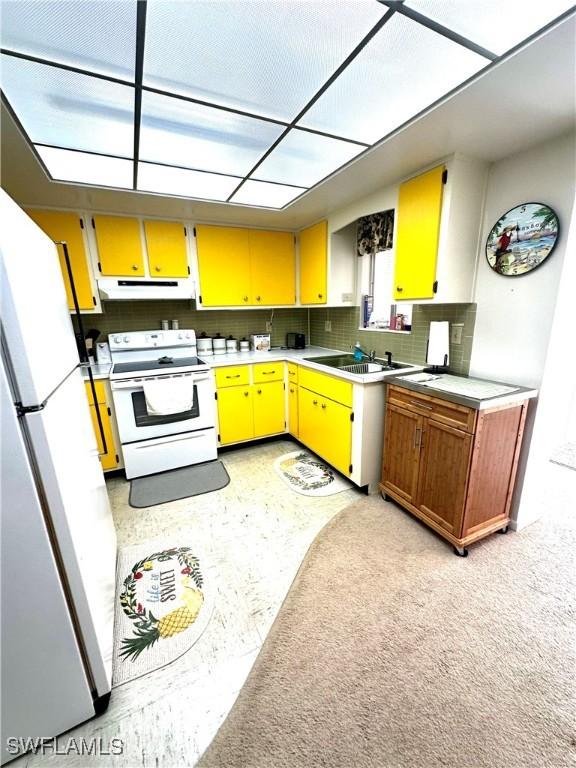 kitchen with backsplash, light carpet, sink, and white appliances