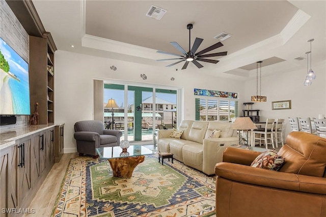 living room featuring ceiling fan, french doors, crown molding, light hardwood / wood-style floors, and a tray ceiling