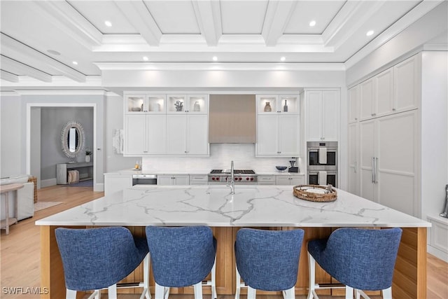 kitchen with light stone countertops, appliances with stainless steel finishes, a spacious island, beam ceiling, and white cabinetry