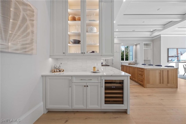 bar with white cabinets, decorative backsplash, light stone countertops, and beverage cooler