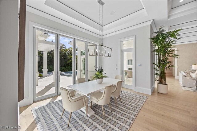 dining space featuring a notable chandelier, a raised ceiling, light wood-type flooring, and french doors