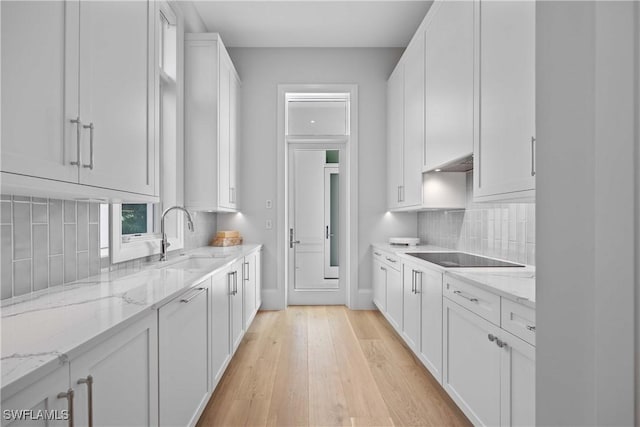 kitchen with white cabinets, sink, light hardwood / wood-style flooring, black electric cooktop, and light stone counters