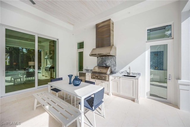 interior space with wooden ceiling, backsplash, wall chimney range hood, sink, and white cabinetry