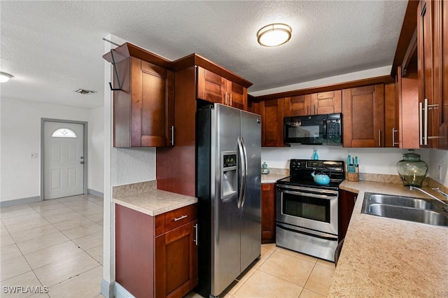 kitchen featuring sink, light tile patterned floors, a textured ceiling, and appliances with stainless steel finishes