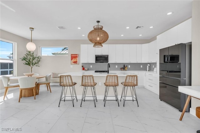 kitchen with decorative backsplash, a kitchen island with sink, sink, white cabinets, and hanging light fixtures