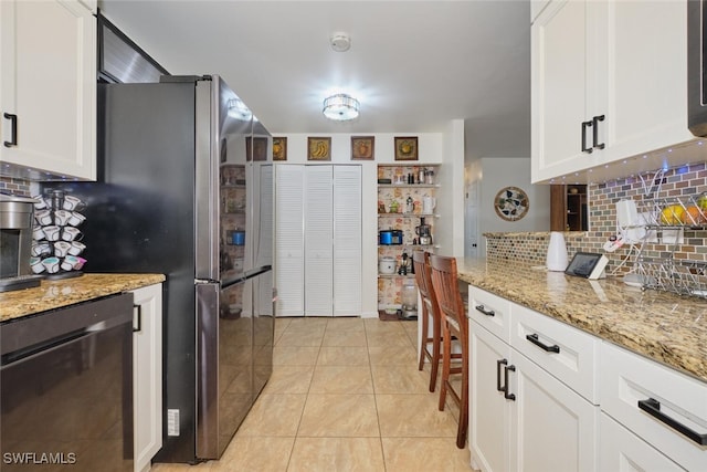 kitchen featuring light tile patterned floors, tasteful backsplash, light stone counters, stainless steel dishwasher, and white cabinets