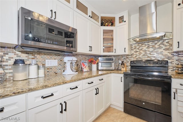 kitchen with light stone countertops, wall chimney exhaust hood, backsplash, black / electric stove, and white cabinets