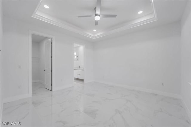 unfurnished bedroom featuring a raised ceiling, a closet, a spacious closet, and ceiling fan