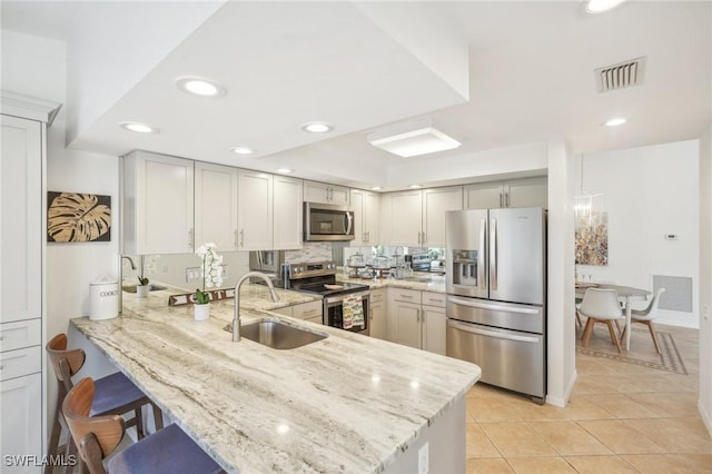 kitchen featuring sink, light tile patterned floors, appliances with stainless steel finishes, light stone counters, and kitchen peninsula