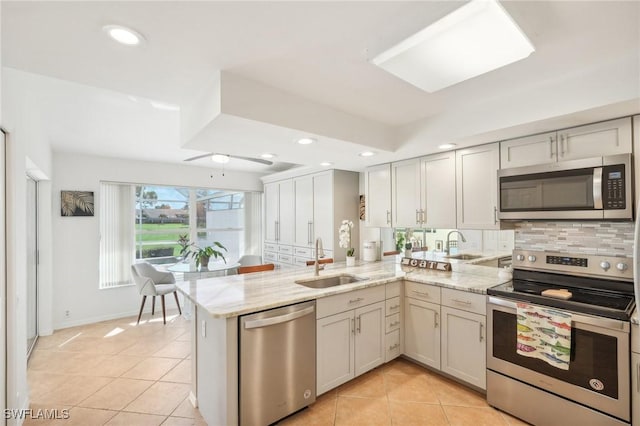 kitchen featuring kitchen peninsula, appliances with stainless steel finishes, light stone counters, sink, and light tile patterned floors