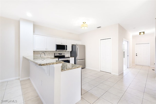 kitchen with kitchen peninsula, decorative backsplash, light stone counters, white cabinetry, and stainless steel appliances