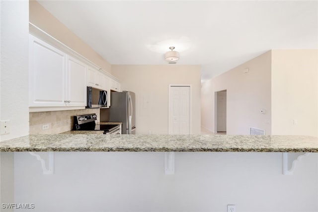 kitchen featuring white cabinets, stainless steel appliances, kitchen peninsula, and light stone countertops