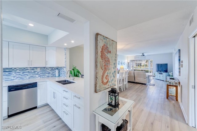 kitchen featuring sink, white cabinetry, stainless steel dishwasher, light hardwood / wood-style floors, and backsplash