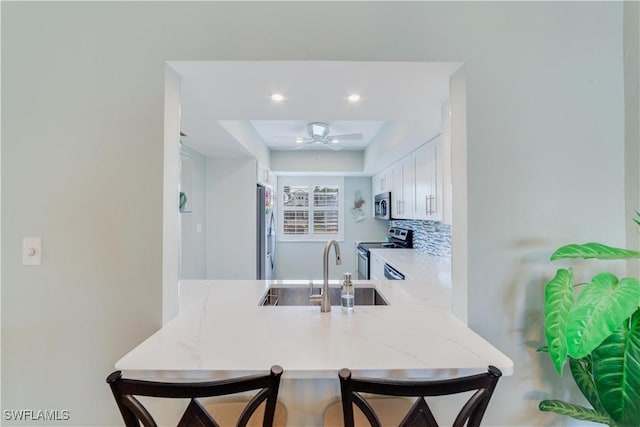 kitchen with sink, white cabinets, decorative backsplash, kitchen peninsula, and stainless steel appliances