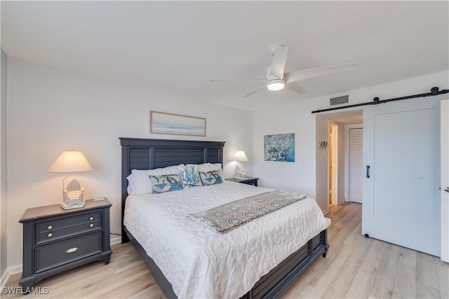 bedroom featuring a barn door, ceiling fan, and light wood-type flooring