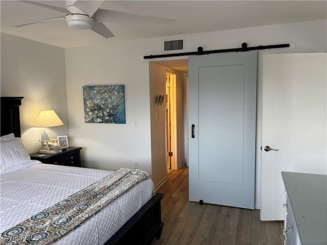 bedroom featuring a barn door, hardwood / wood-style floors, and ceiling fan