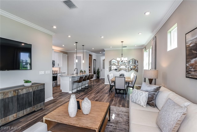 living room with dark hardwood / wood-style floors, an inviting chandelier, ornamental molding, and sink