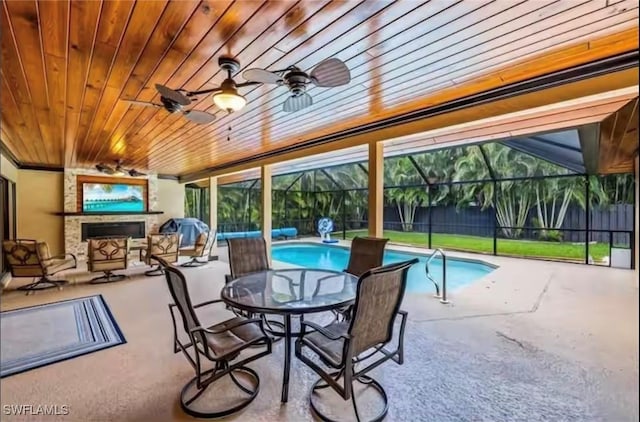 view of swimming pool featuring ceiling fan, a large fireplace, a patio area, and glass enclosure