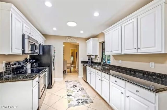 kitchen with stainless steel appliances, light tile patterned flooring, dark stone counters, white cabinets, and sink