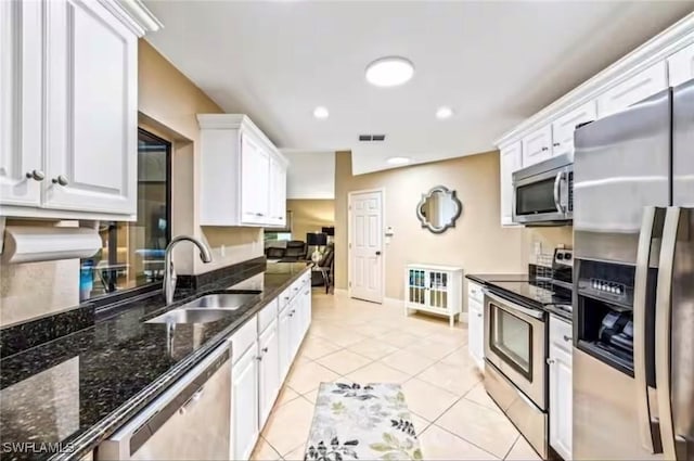 kitchen featuring white cabinetry, stainless steel appliances, dark stone counters, sink, and light tile patterned floors