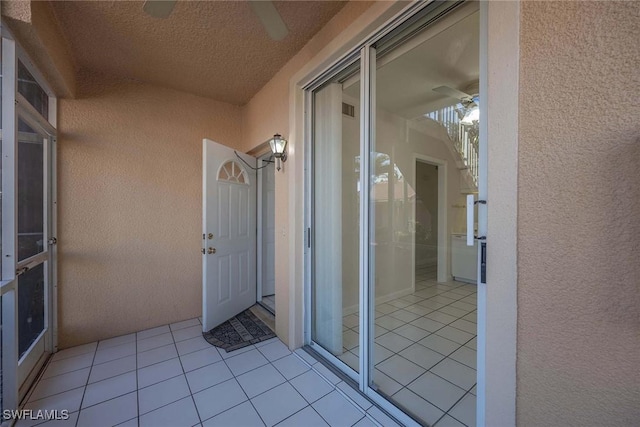 exterior space featuring a textured wall, tile patterned flooring, and a ceiling fan