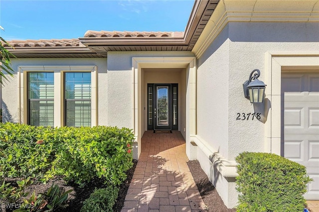 property entrance featuring a tiled roof, an attached garage, and stucco siding