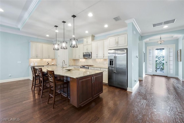 kitchen featuring light stone counters, dark hardwood / wood-style flooring, an island with sink, decorative light fixtures, and appliances with stainless steel finishes