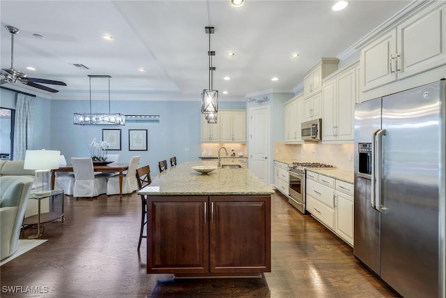 kitchen with premium appliances, light stone counters, decorative light fixtures, a kitchen island with sink, and a breakfast bar