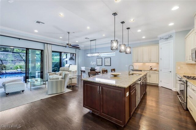 kitchen with sink, stainless steel gas range oven, backsplash, decorative light fixtures, and a center island with sink