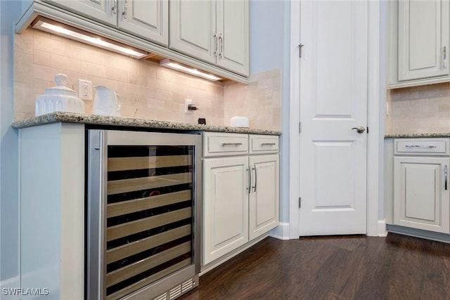 bar with dark wood-type flooring, wine cooler, decorative backsplash, light stone counters, and white cabinetry