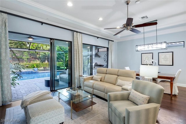 living room with hardwood / wood-style floors, ceiling fan, a raised ceiling, and crown molding