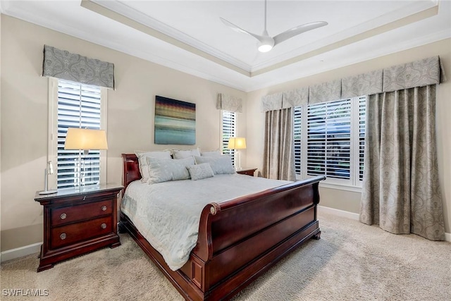 carpeted bedroom with a tray ceiling, multiple windows, ceiling fan, and crown molding