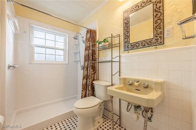 bathroom with toilet, a wainscoted wall, tile walls, a stall shower, and crown molding