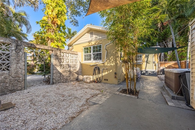 exterior space with a hot tub, fence, a patio, and stucco siding