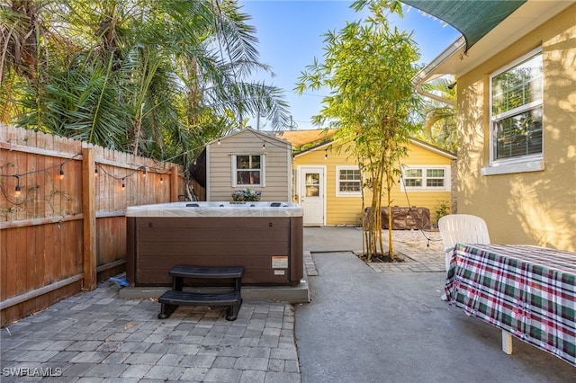 view of patio / terrace with an outbuilding, a fenced backyard, a hot tub, and a storage unit