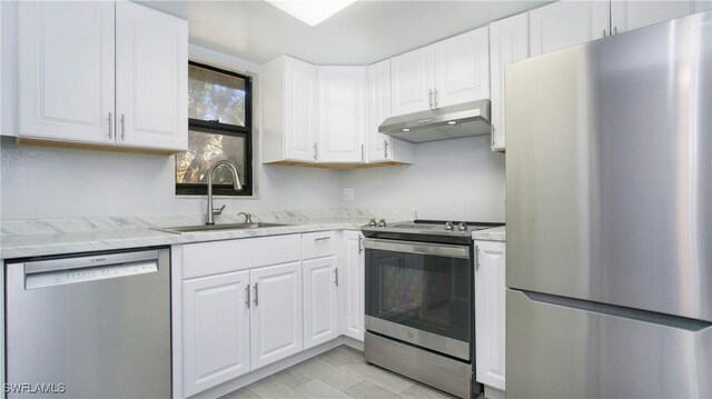 kitchen featuring sink, light stone countertops, light wood-type flooring, appliances with stainless steel finishes, and white cabinetry