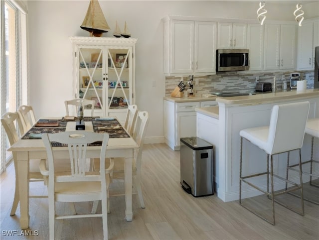 kitchen featuring light wood-type flooring, a kitchen bar, stainless steel microwave, white cabinets, and decorative backsplash