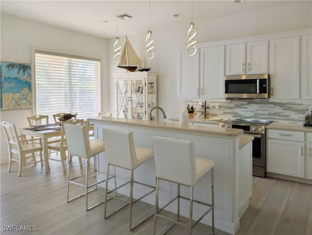 kitchen featuring a kitchen breakfast bar, stainless steel appliances, light wood-style floors, light countertops, and decorative backsplash