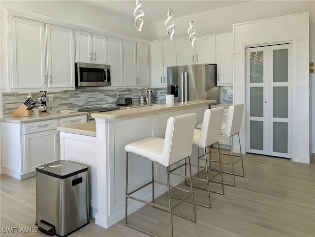 kitchen with stainless steel appliances, white cabinets, light wood finished floors, decorative backsplash, and light countertops