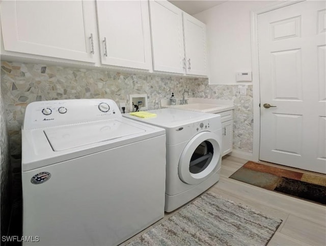 clothes washing area featuring a wainscoted wall, light wood finished floors, cabinet space, a sink, and independent washer and dryer