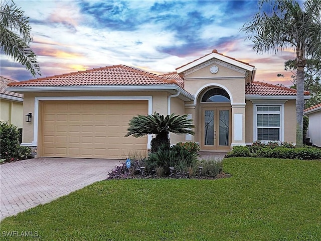 mediterranean / spanish home featuring an attached garage, french doors, a yard, and stucco siding