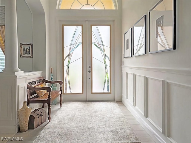 doorway featuring french doors, decorative columns, wainscoting, and a decorative wall